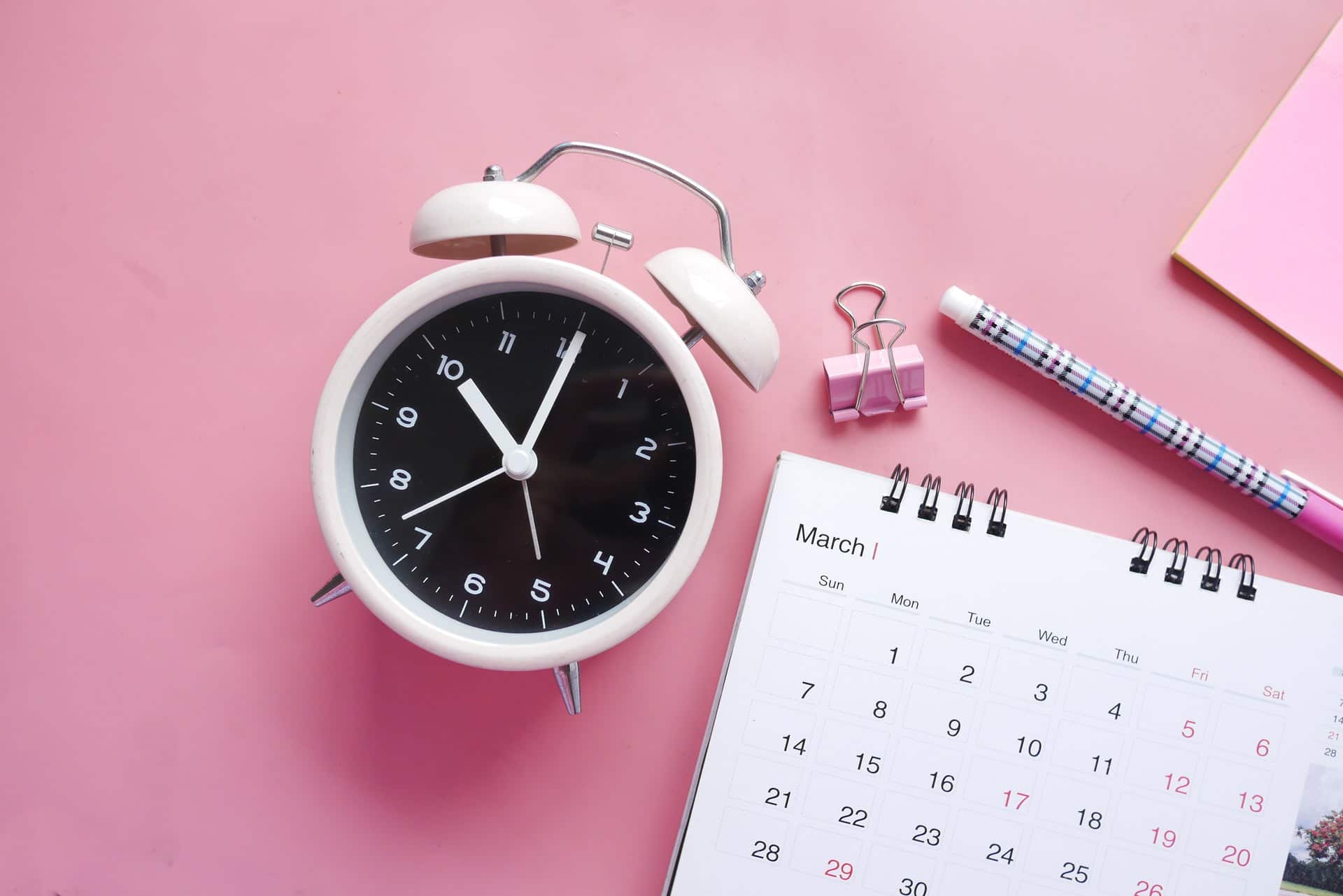 calendar, marker, clock on pink table