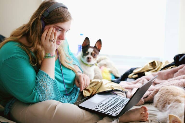 A socially isolated girl learning from laptop while her dog sits beside