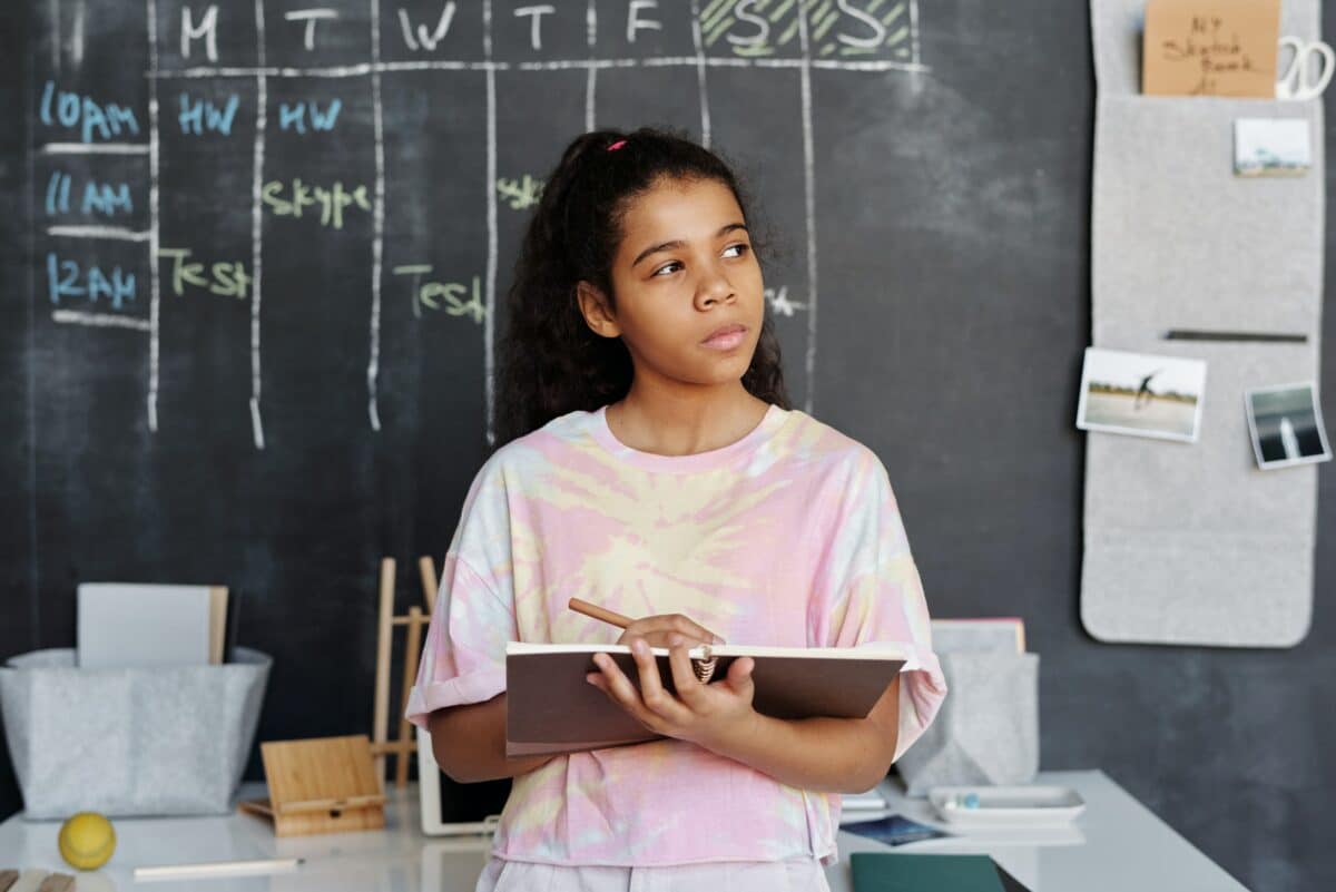 A girl thinking while holding a notebook and pen