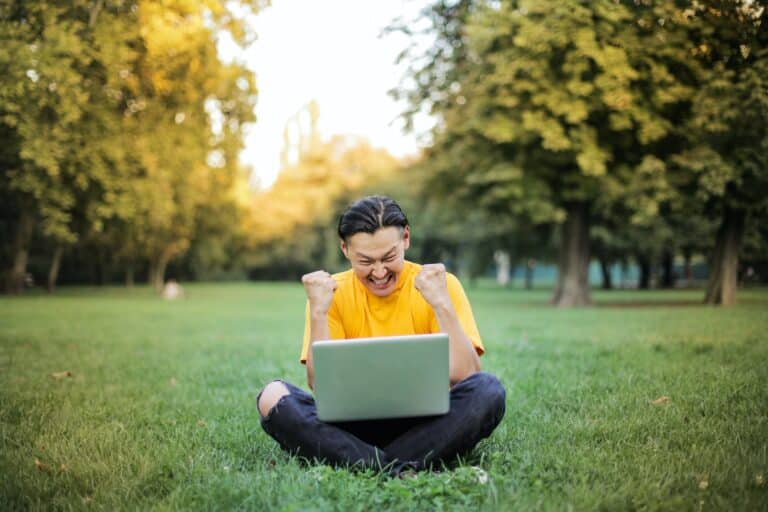 A happy guy sitting on grass with laptop