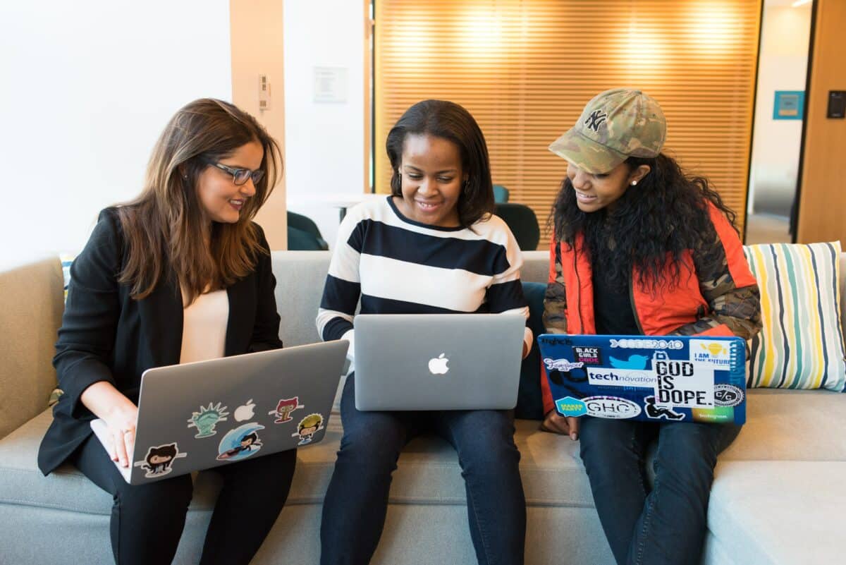 Three women sitting while holding their laptops